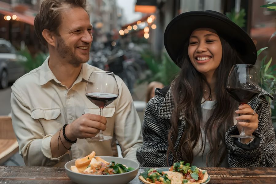 The Amber at Greenbrier A man and woman smiling and toasting red wine at an outdoor restaurant table with food.