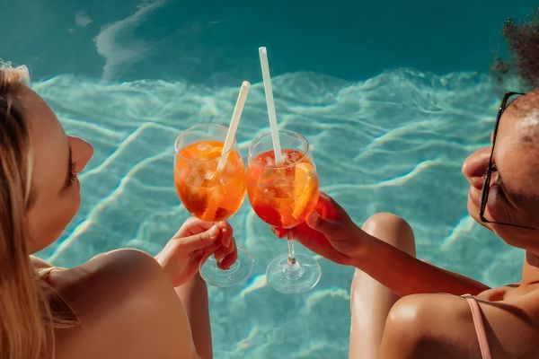 The Amber at Greenbrier Two women sitting by a pool, clinking glasses of orange cocktails with straws.