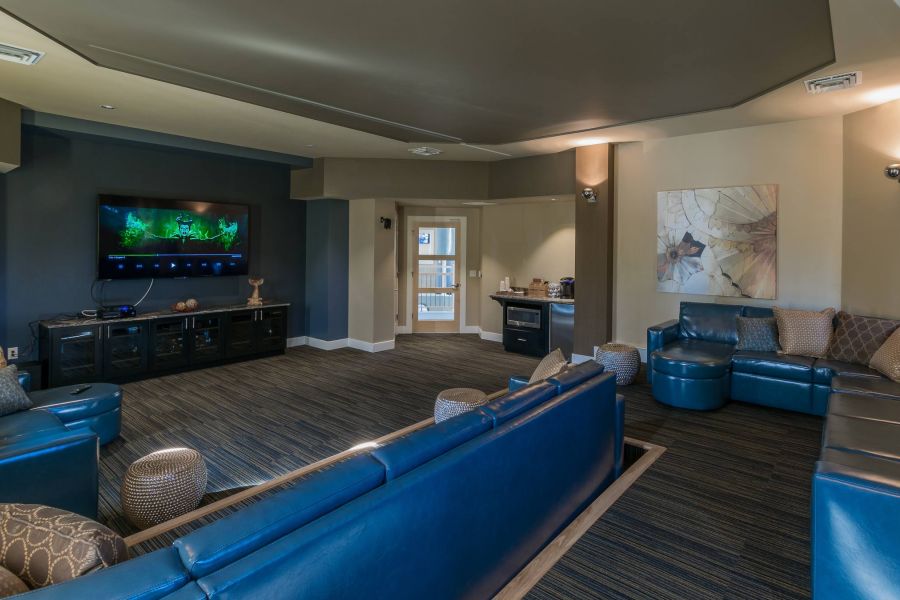 The Amber at Greenbrier Modern lounge with blue leather sofas, wall-mounted TV, and decorative wall art, featuring soft lighting.