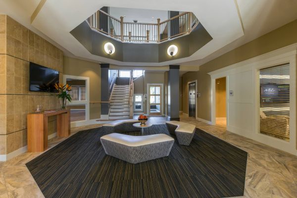 The Amber at Greenbrier Modern lobby with geometric seating, a central table, staircase, elevators, and natural light from large windows.