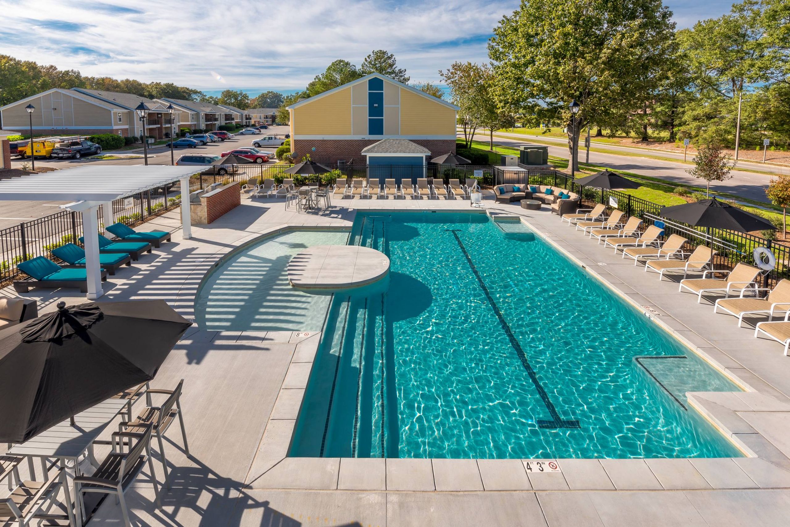 The Amber at Greenbrier Outdoor swimming pool with lounge chairs, umbrellas, and shaded seating area at an apartment complex.