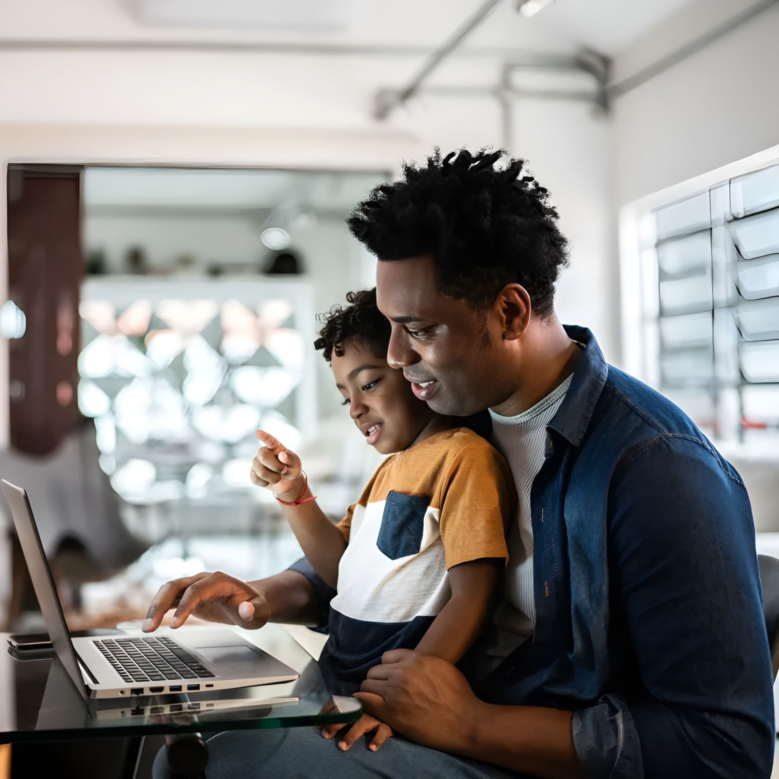 The Amber at Greenbrier A father and son smiling and using a laptop together at home.