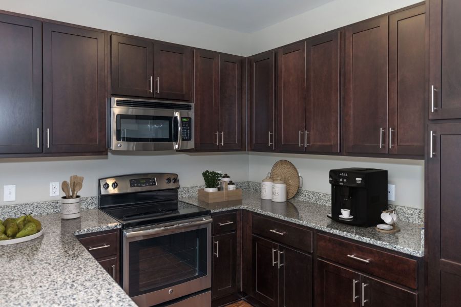 Modern kitchen with dark wood cabinets, granite countertops, a stove, microwave, and a coffee machine.
