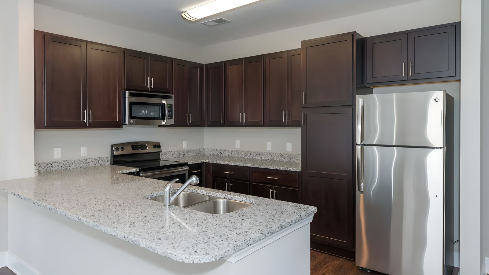 Modern kitchen and living area with white cabinets, stainless steel appliances, and a large island. Cozy seating area with a sofa and rug in the background. Bright and inviting atmosphere.