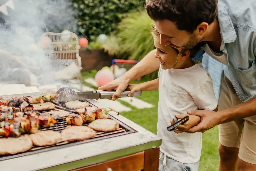 The Amber at Greenbrier A man and child grill skewers and meat together at an outdoor barbecue in a backyard.
