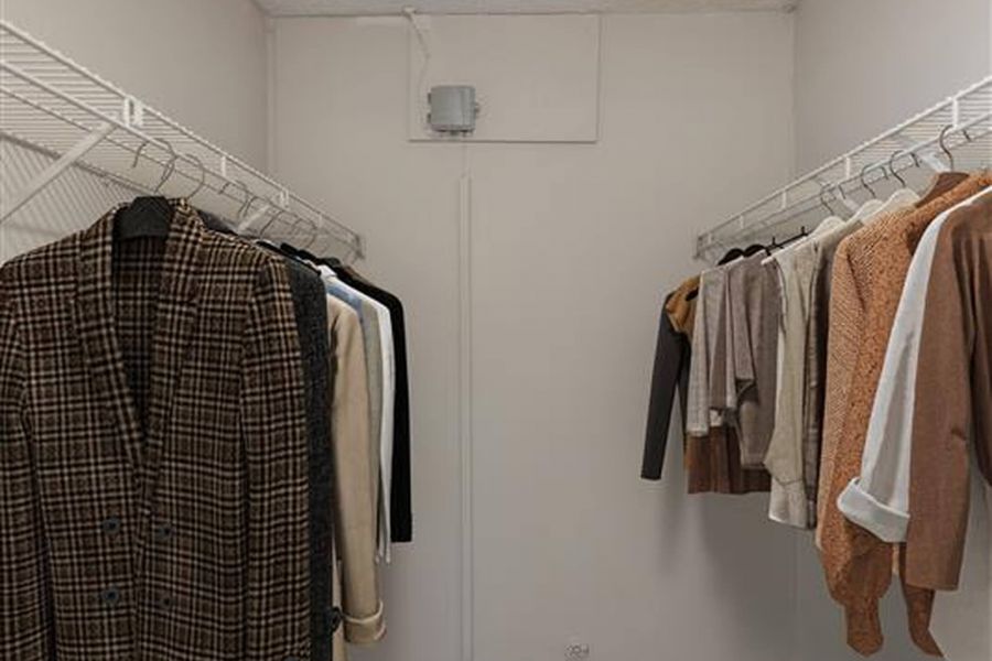 Walk-in closet with clothes hanging on both sides, shoes on the floor, and a basket in the corner.