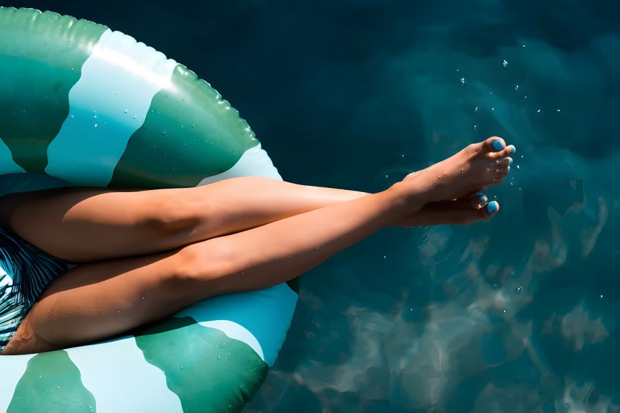 The Amber at Greenbrier Person relaxing in a green striped pool float on blue water, legs crossed and toes touching the surface.