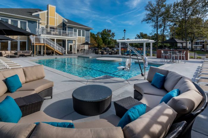 The Amber at Greenbrier Modern outdoor pool area with lounge chairs, sofas, and tables, surrounded by buildings and trees.