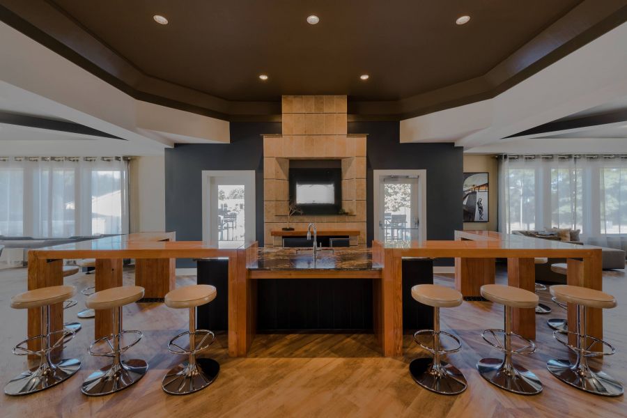 The Amber at Greenbrier Modern kitchen with wooden island, bar stools, built-in sink, and wall-mounted TV under recessed lighting.