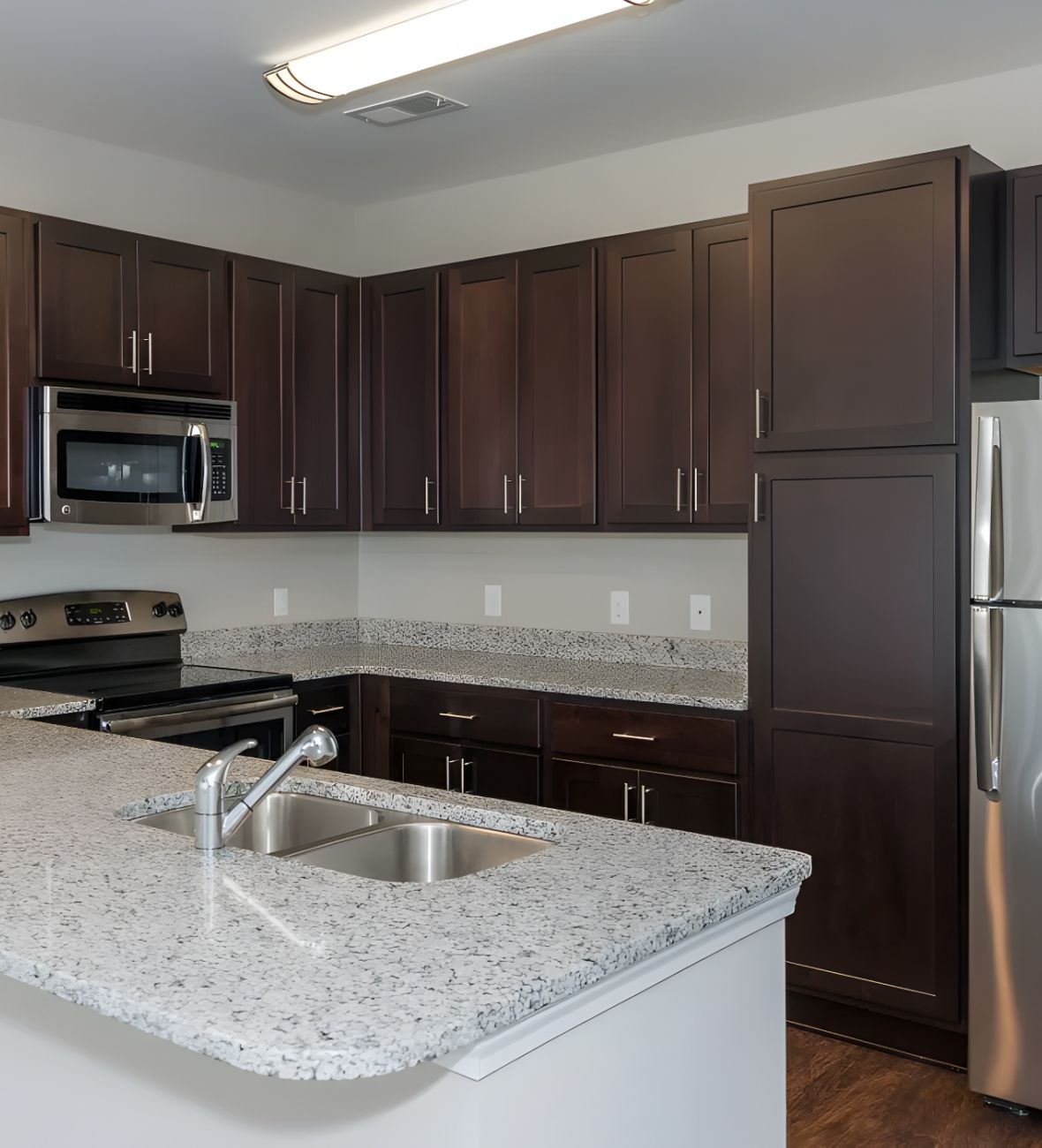 The Amber at Greenbrier Modern kitchen with dark cabinets, stainless steel appliances, and light granite countertops.